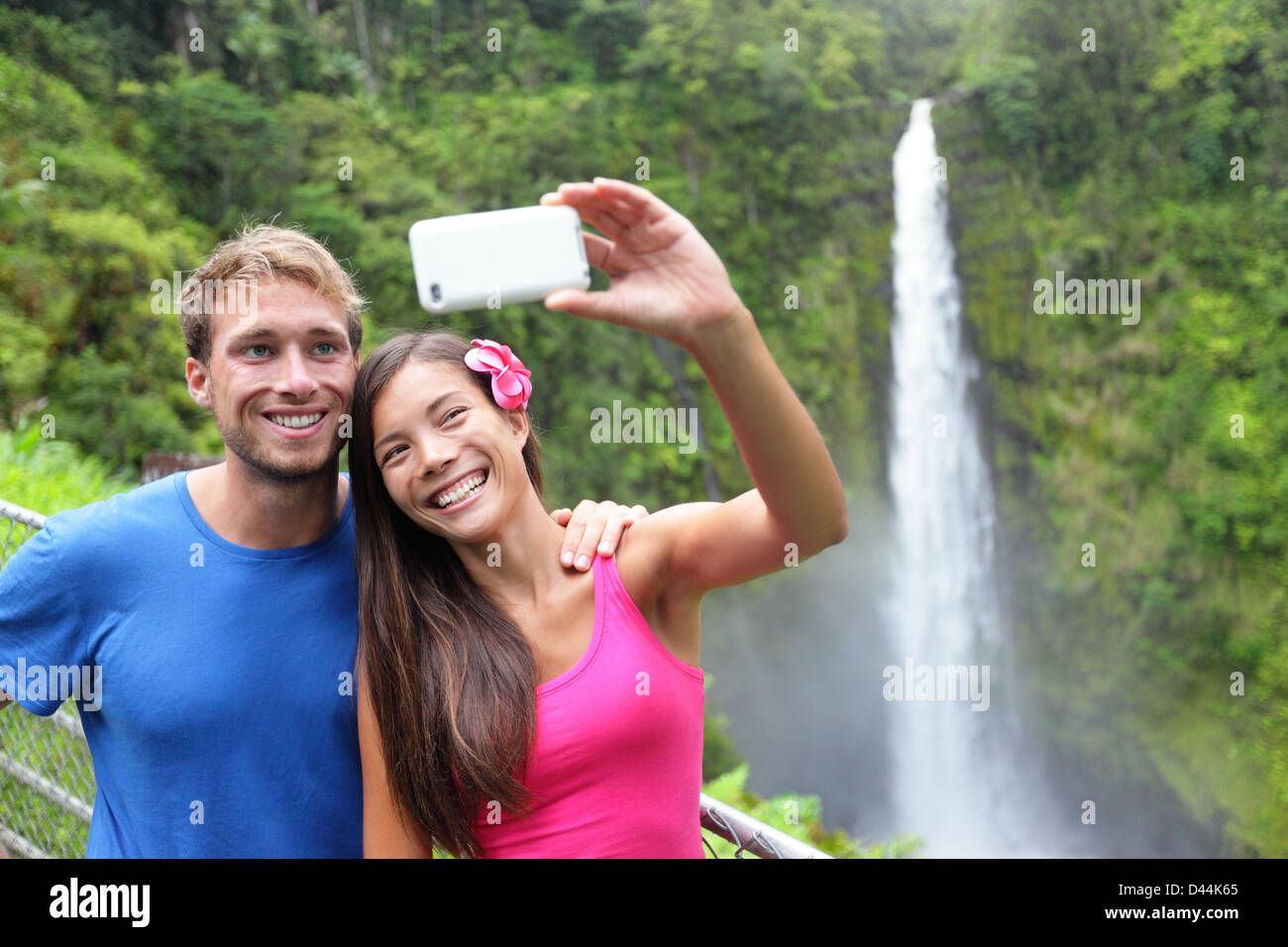 Felice giovane coppia multietnica tenendo autoritratto foto con la fotocamera del telefono alle Hawaii, grandi isole, Akaka Falls Foto Stock