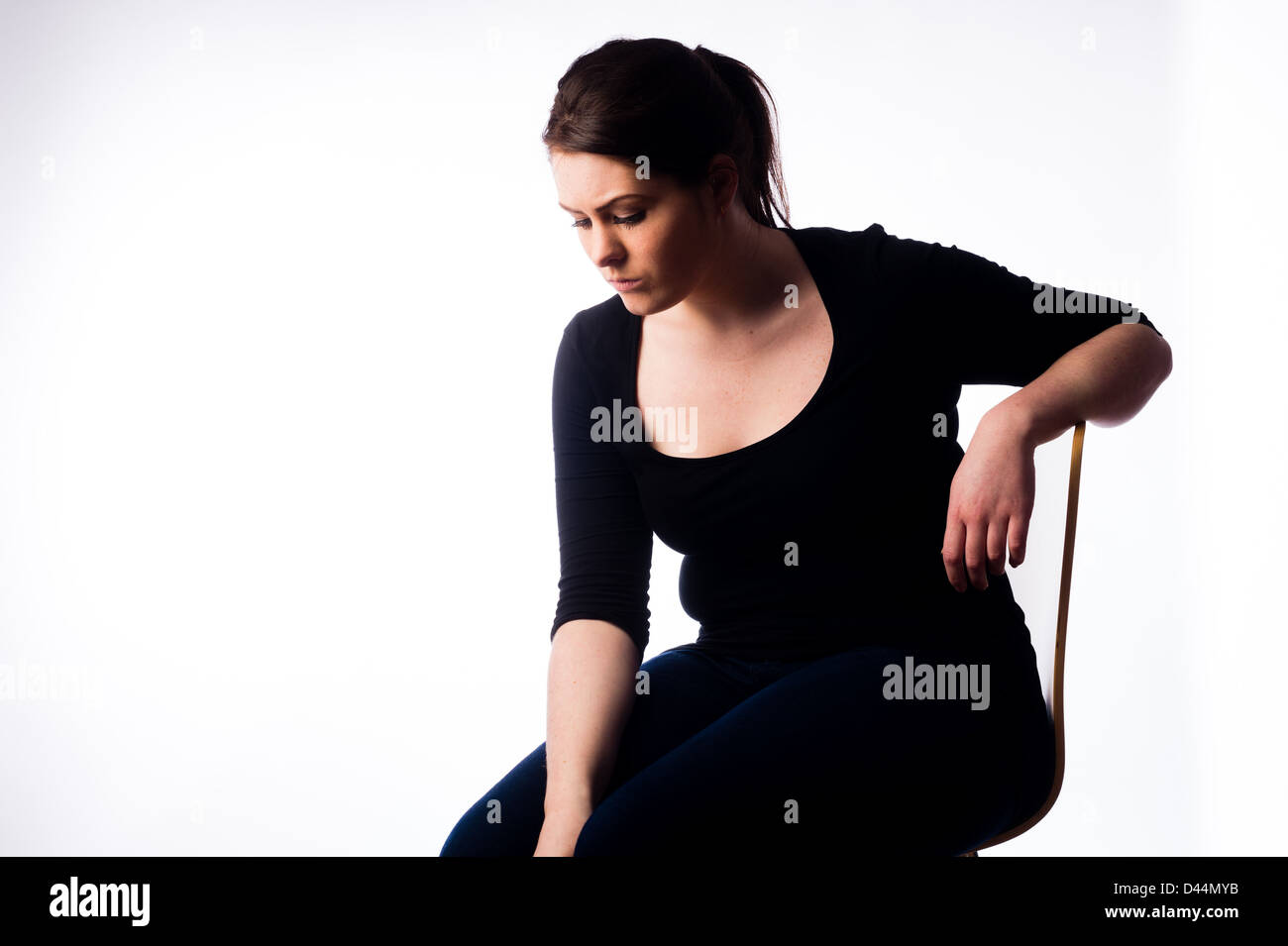 Una giovane donna, marrone capelli, seduto da solo, guardando triste giù premuto lonely REGNO UNITO Foto Stock