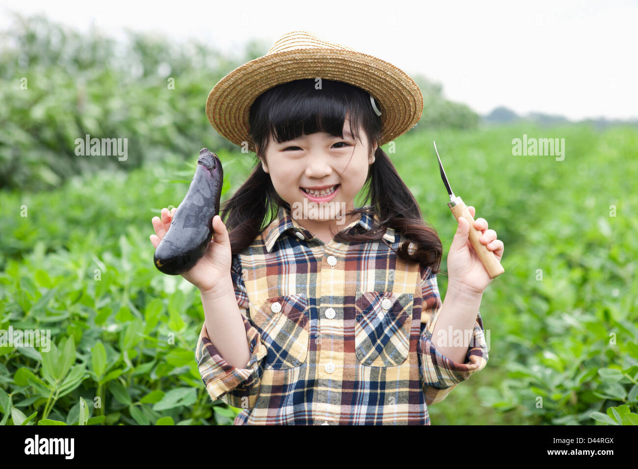 Una ragazza in dell'agricoltore hat in posa con le melanzane Foto Stock