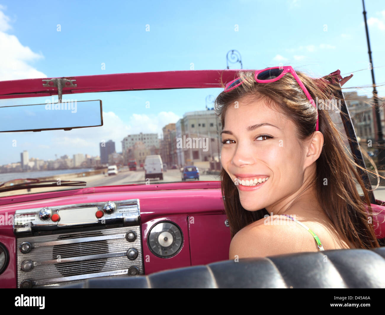 Ritratto di giovane felice razza mista Asian / Caucasian sul sedile del passeggero in rosa vintage auto convertibili, Havana, Cuba Foto Stock