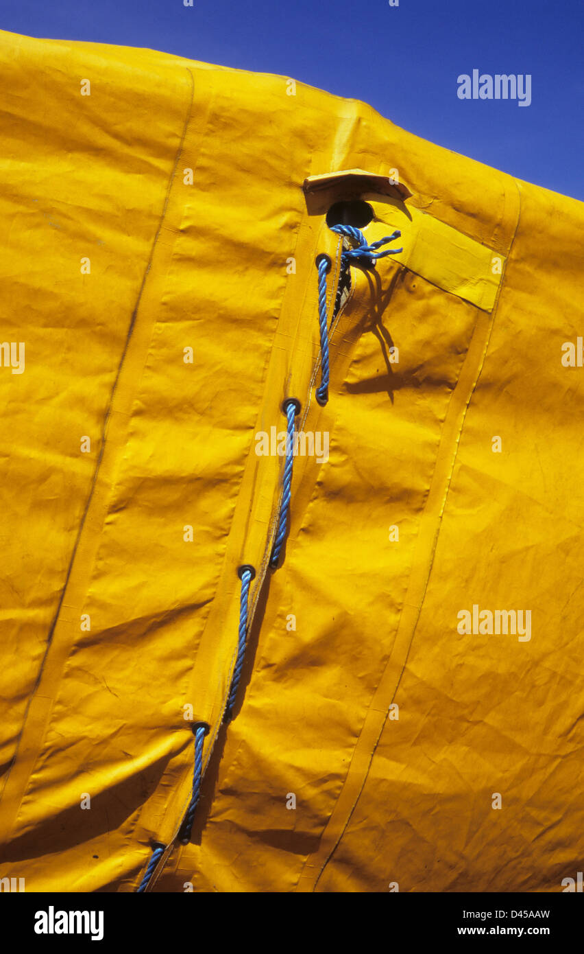 Dettaglio di due luminose in plastica gialla fogli telone cucite assieme con nylon blu corda sotto il profondo blu del cielo Foto Stock