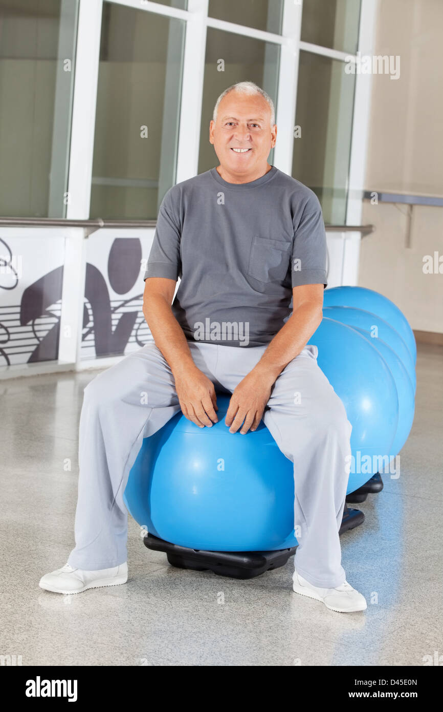 Senior uomo seduto su blu palla nel centro fitness Foto Stock