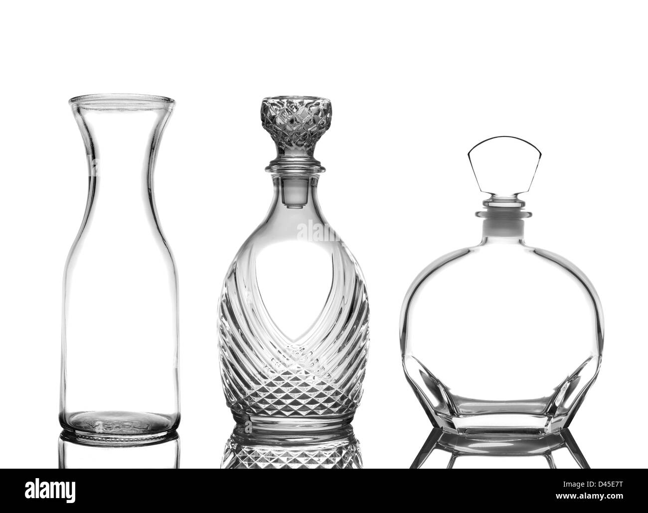 Primo piano di tre decantatori di vetro su bianco con riflessi. Caraffa di vino e cognac decanter vengono raffigurati. Foto Stock