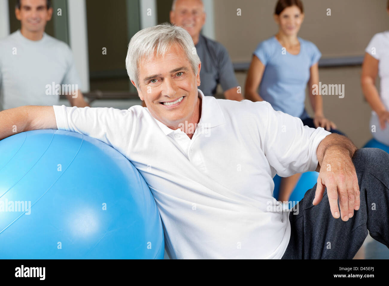 Felice uomo anziano seduto accanto a palla nel centro fitness Foto Stock