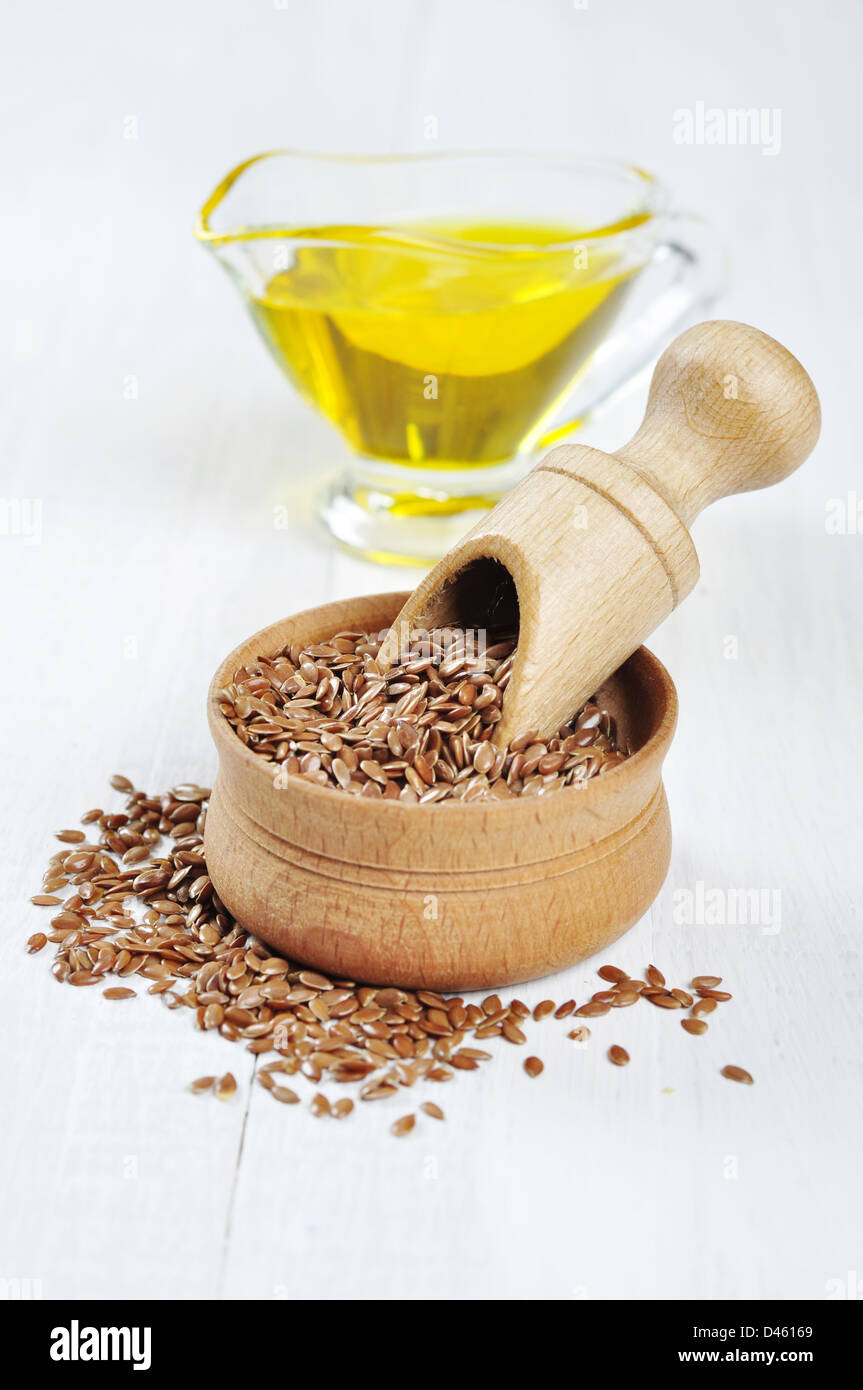 Ciotola di legno marrone con semi di lino e olio di semi di lino bianco su sfondo di legno Foto Stock