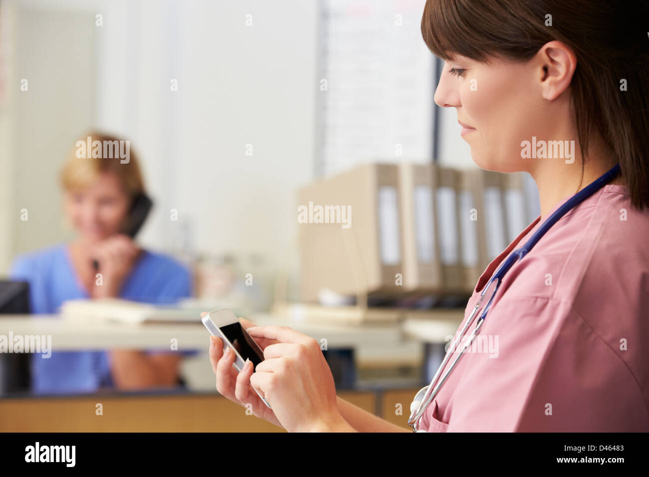 L'infermiera utilizzando il telefono cellulare alla stazione di infermieri Foto Stock