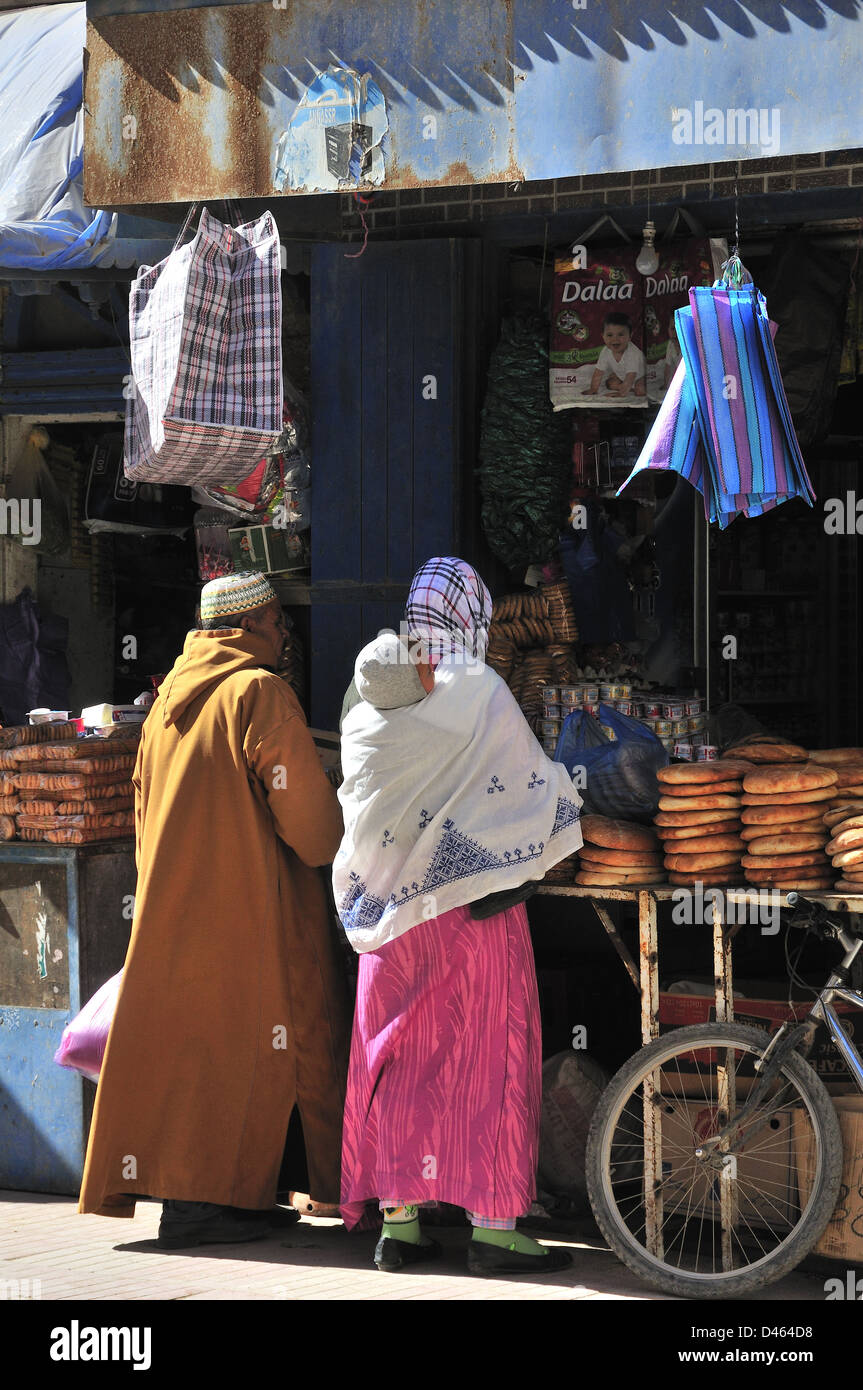 La famiglia marocchina con il bambino in fionda su madre torna l'acquisto di cibo da stallo nella strada principale di Essaouira, Marocco Foto Stock
