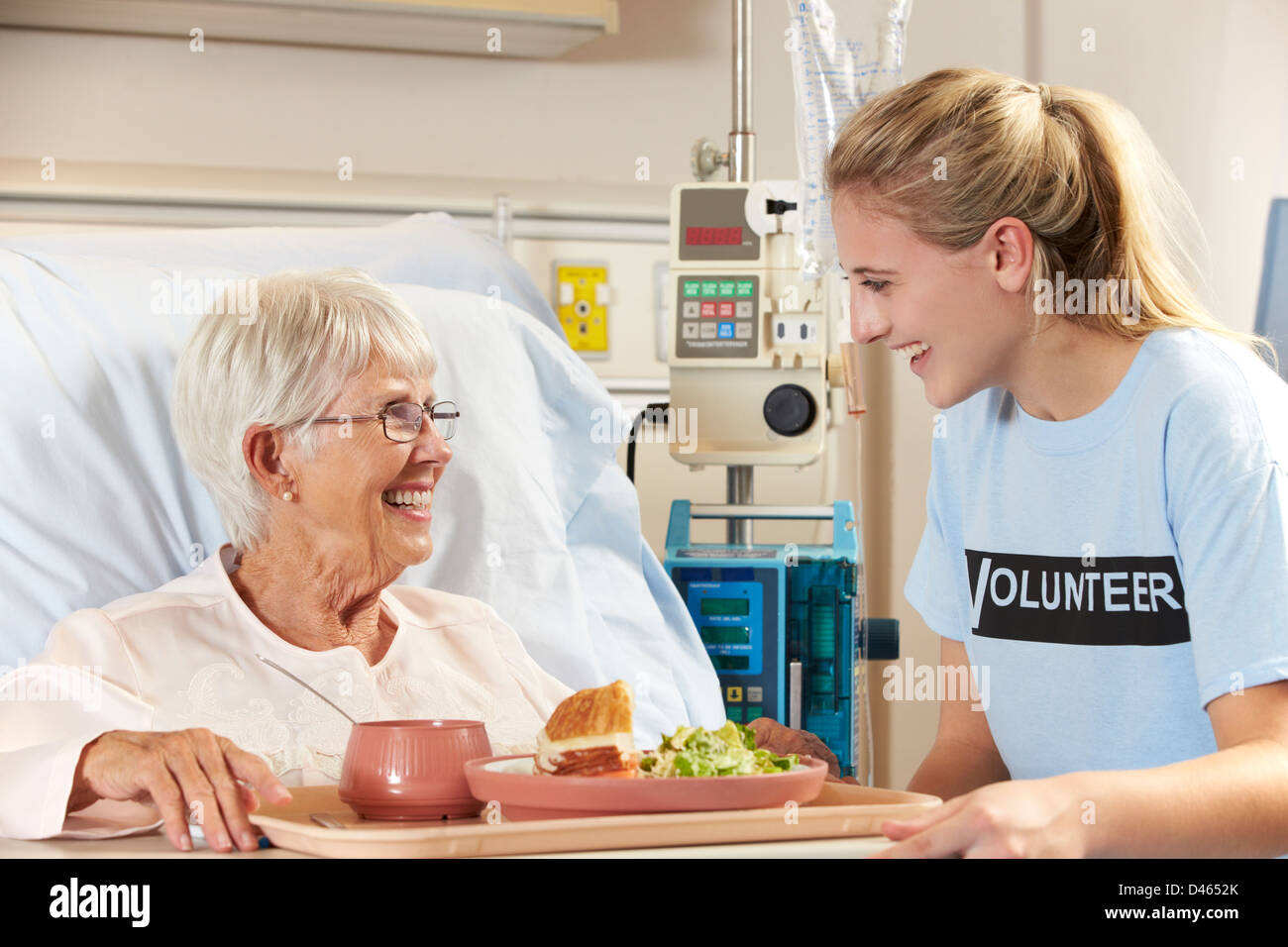Volontario di adolescenti che serve Senior paziente femmina pasto nel letto di ospedale Foto Stock