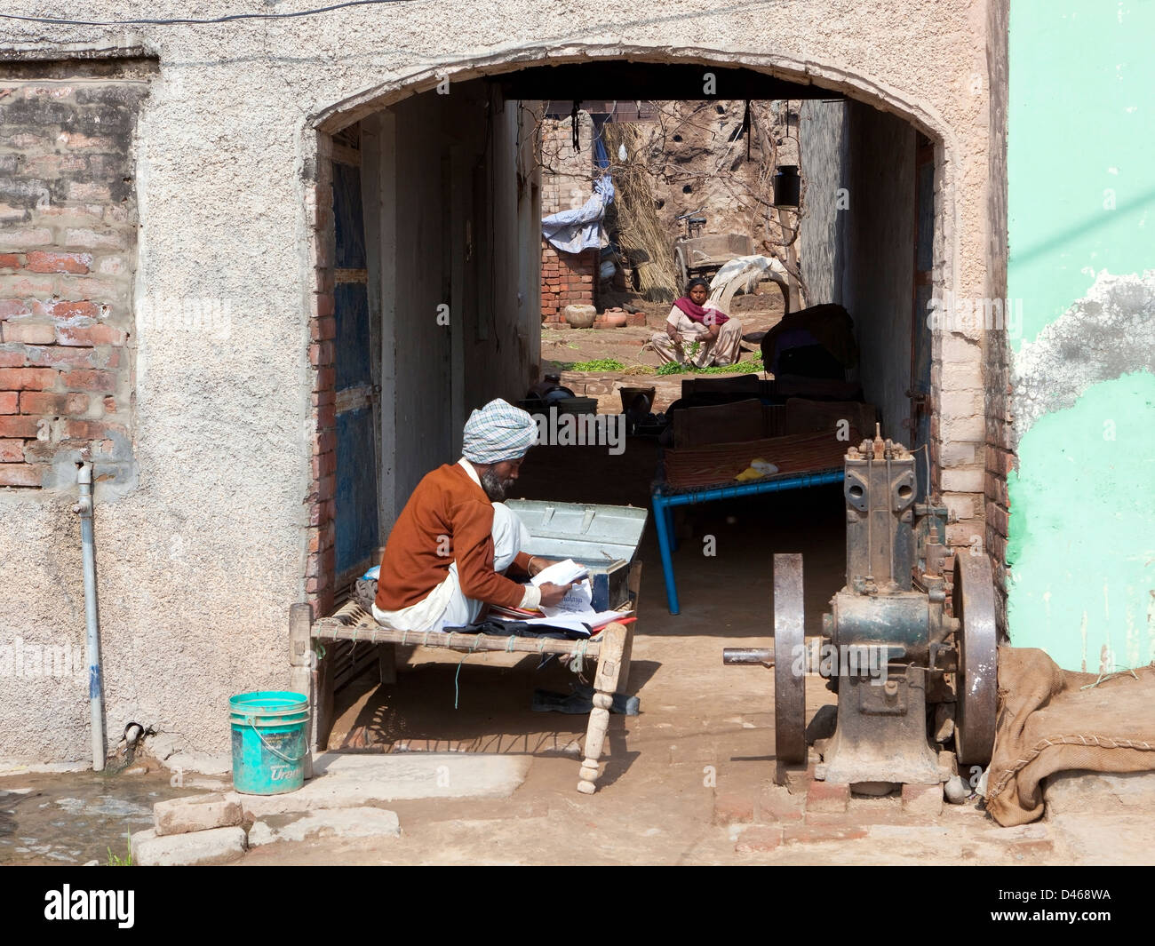 Scena di strada in un piccolo borgo rurale con un uomo seduto fuori di casa sua su un lettino a studiare le carte da una scatola Foto Stock