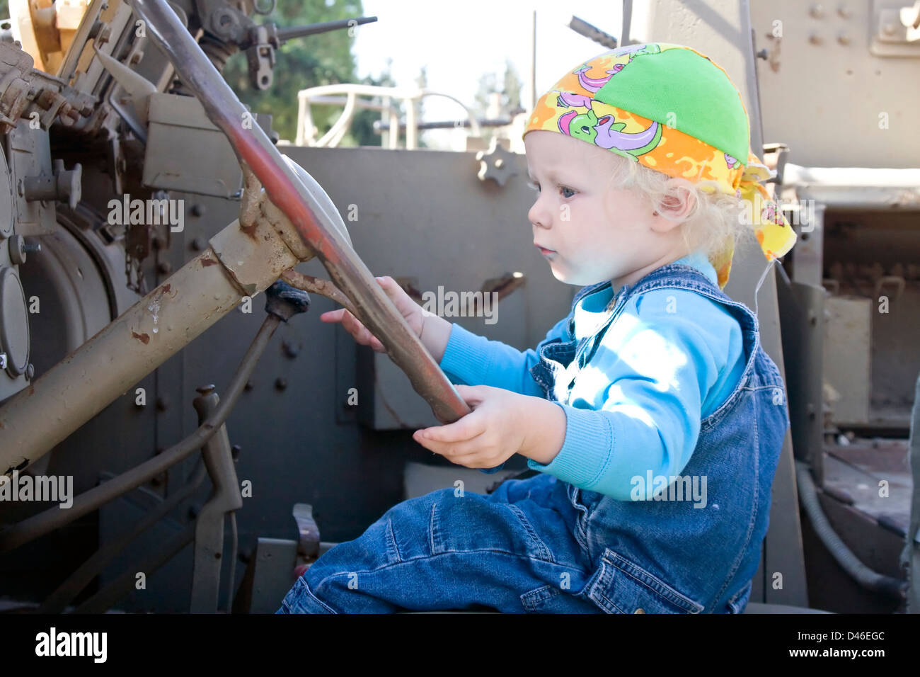 Carino bionda bambina in corrispondenza di una ruota motrice di un vecchio veicolo armor. Foto Stock
