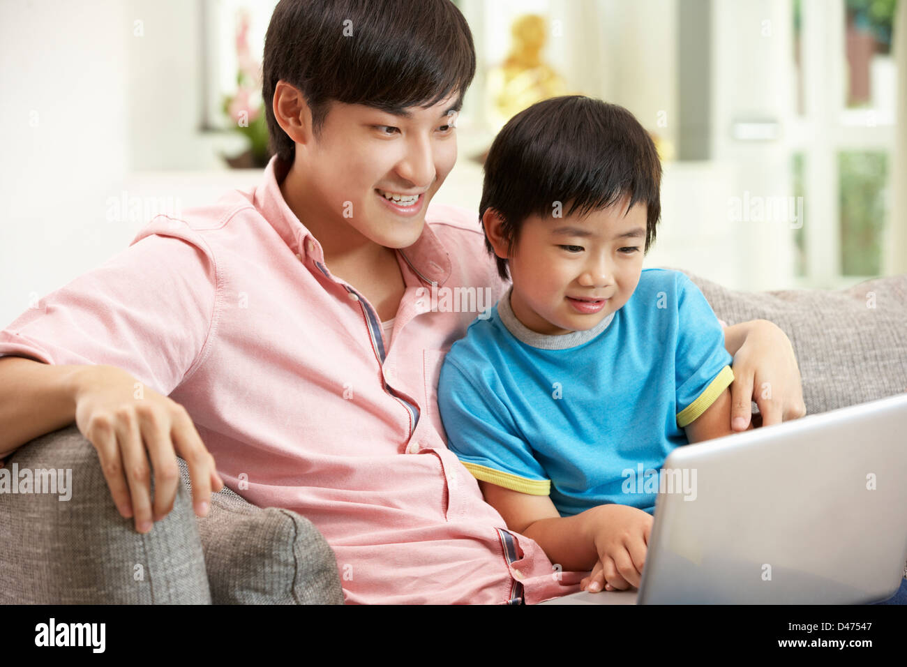 Cinesi padre e figlio utilizzando laptop mentre vi rilassate sul divano di casa Foto Stock