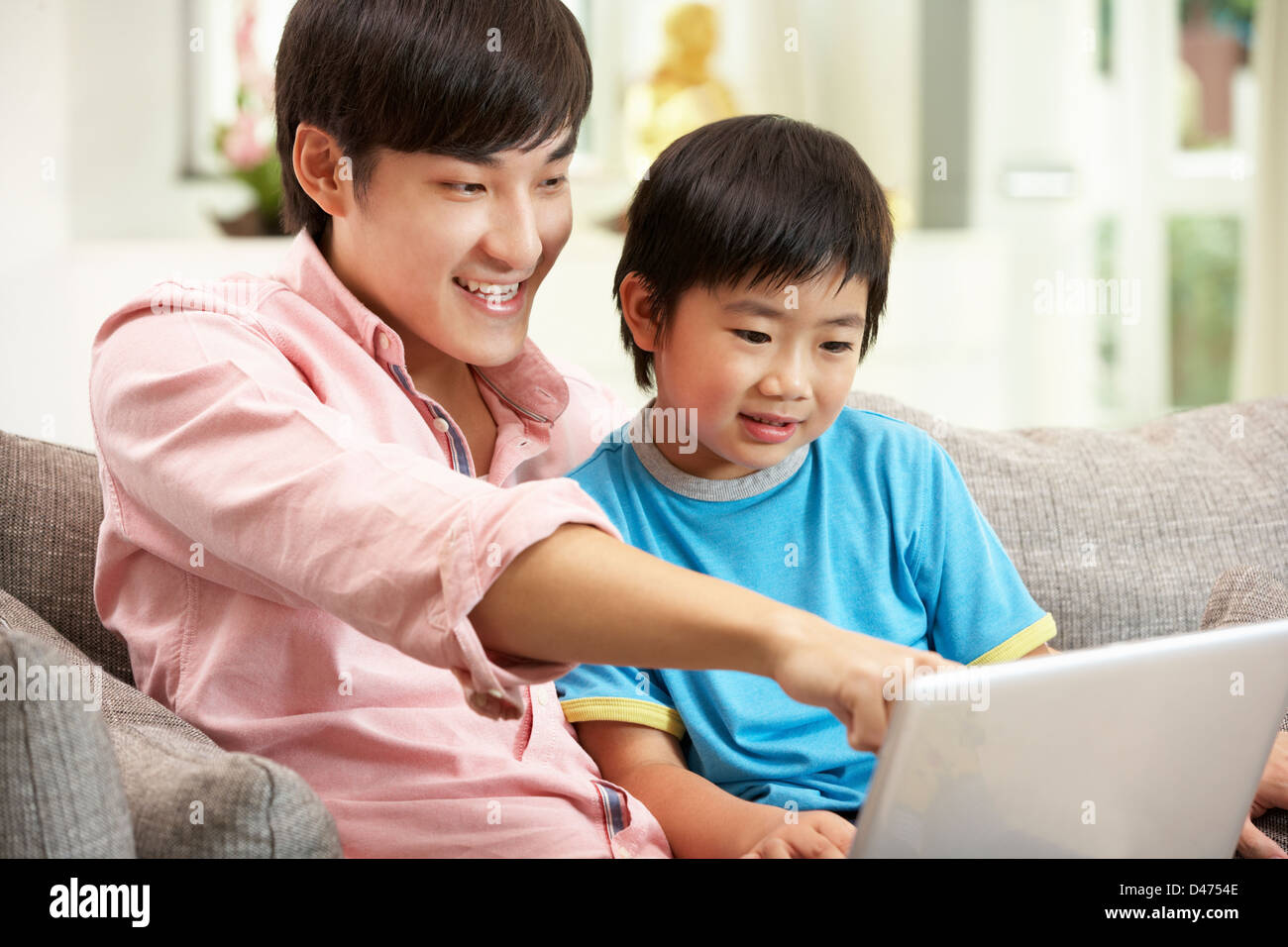 Cinesi padre e figlio utilizzando laptop mentre vi rilassate sul divano di casa Foto Stock