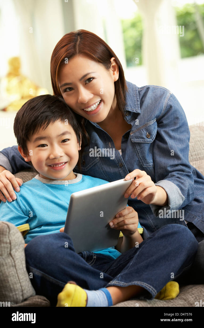 Madre cinese e figlio utilizzando computer tavoletta mentre seduto sul divano di casa Foto Stock