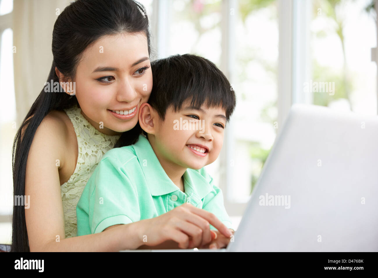 Madre cinese e figlio seduti alla scrivania con computer portatile a casa Foto Stock