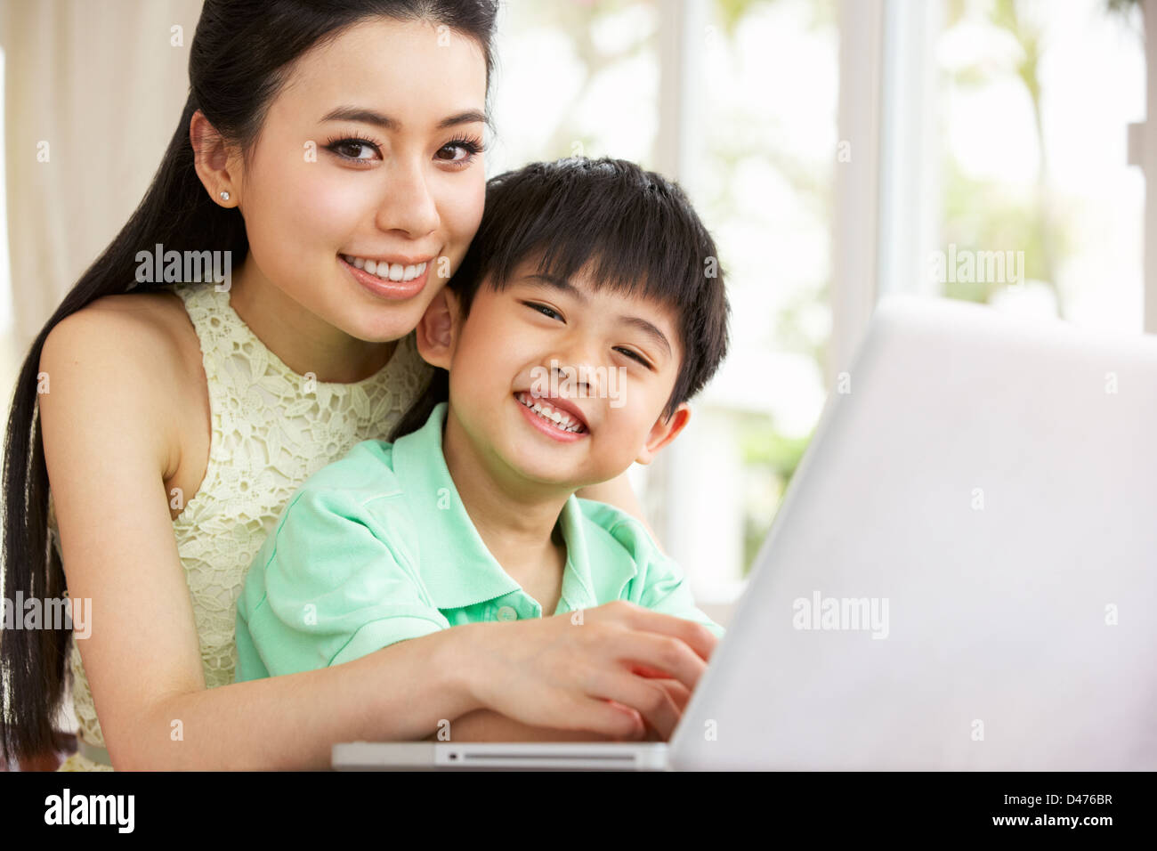 Madre cinese e figlio seduti alla scrivania con computer portatile a casa Foto Stock