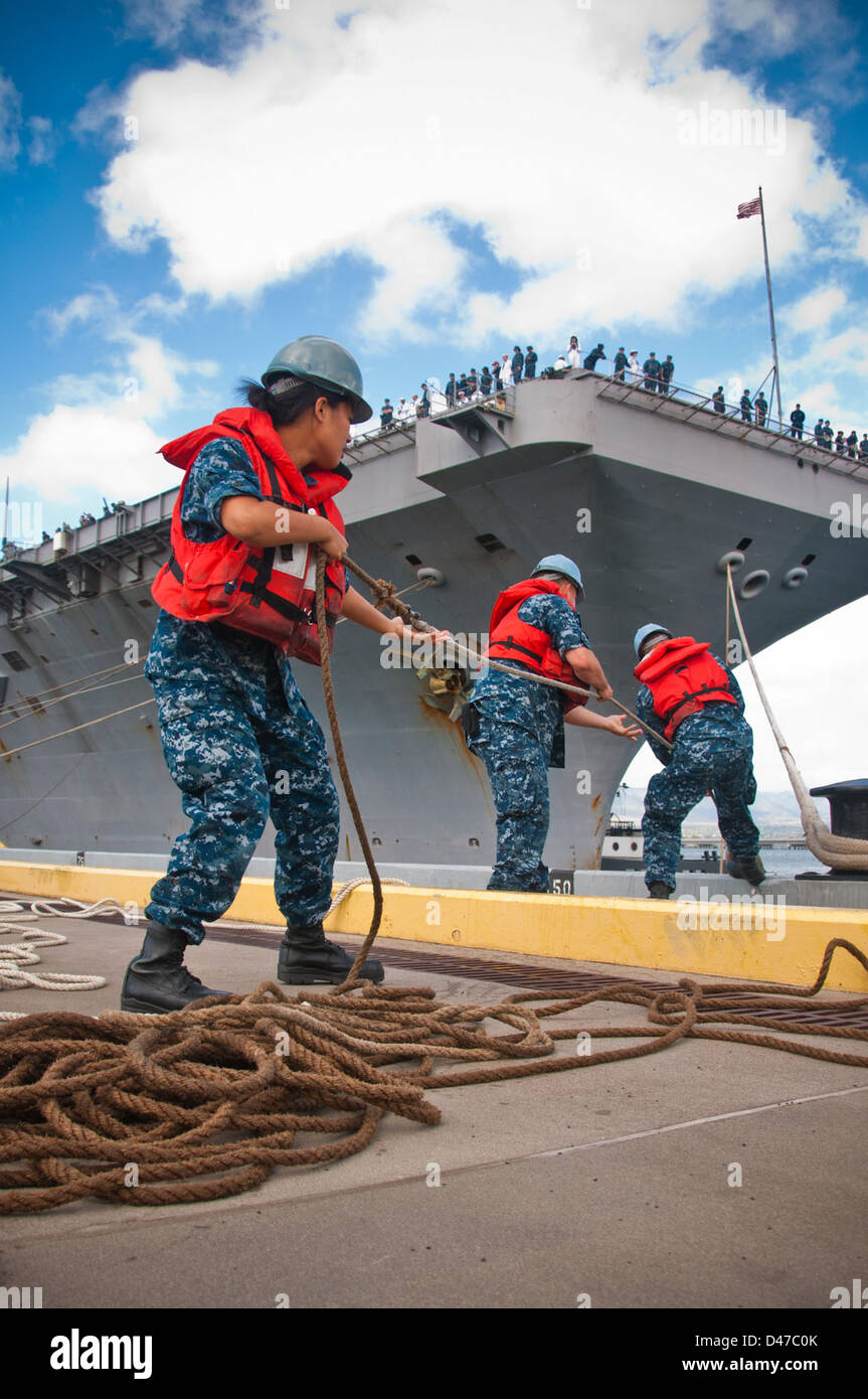I marinai a bordo della portaerei classe Nimitz USS John C. Stennis (CVN 74) lavorano sulle linee di ormeggio mentre la nave arriva alla Joint base Pearl Harbor-Hickam. L'attività garantisce un ancoraggio sicuro e la disponibilità alle operazioni presso la base navale. Foto Stock