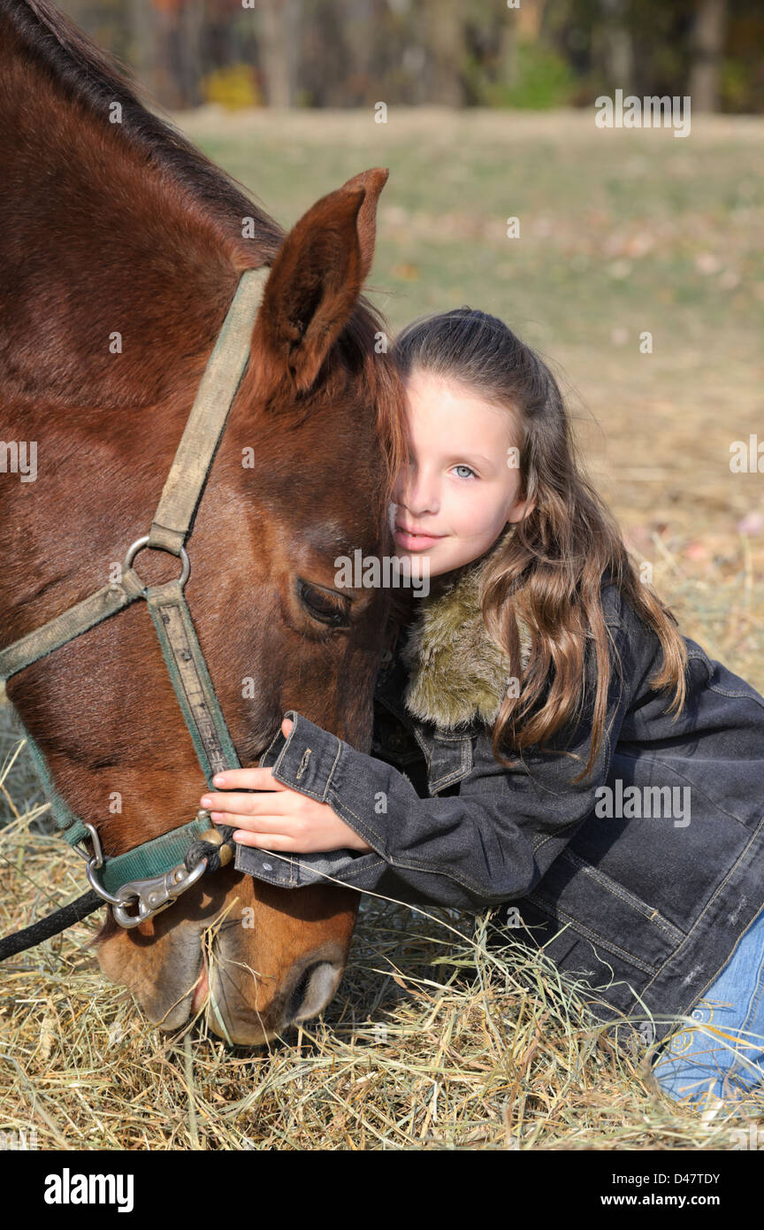 Giovane ragazza abbraccia il suo cavallo strettamente come esso lambisca il fieno, un simpatico otto anni con lunghi capelli bruna. Foto Stock