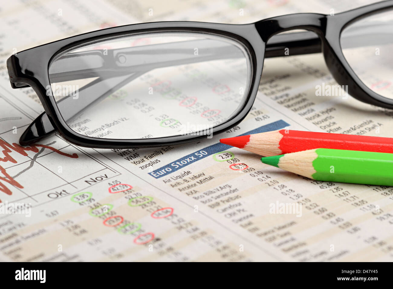 Bicchieri e rosso verde matite sul giornale con grafici azionari Foto Stock