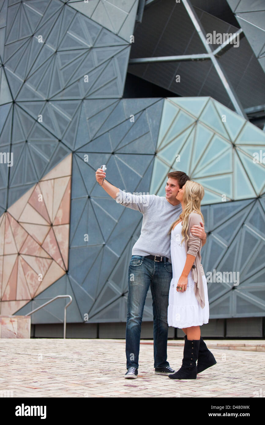 Coppia giovane visite turistiche in città, prendendo un autoritratto. Federation Square, Melbourne, Victoria, Australia Foto Stock