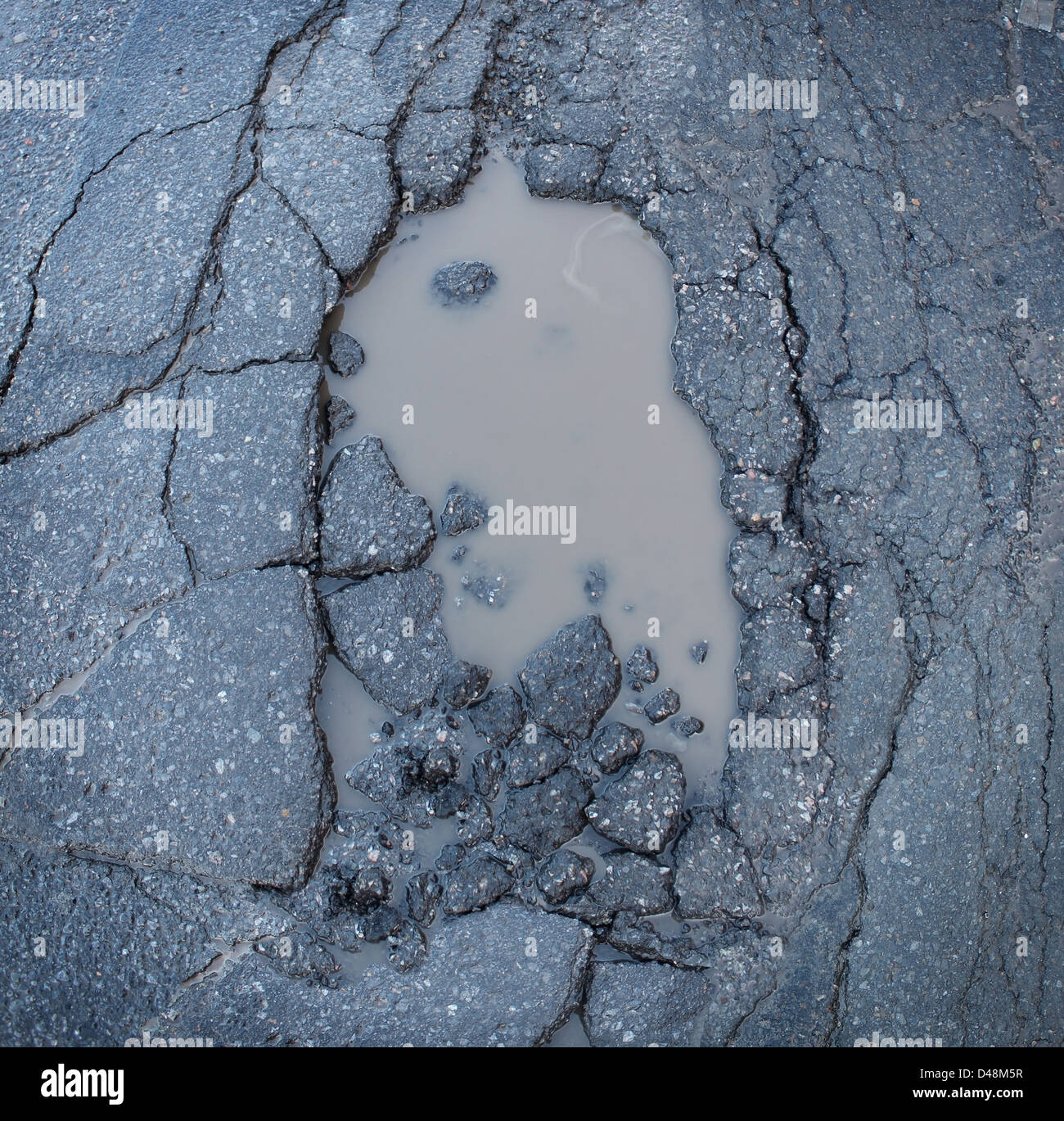 Buca o buca immagine di una rottura asfalto con una sporca pozza d'acqua come un simbolo di trasporto della manutenzione stradale e le auto di assicurazione rischio di sospensioni auto. Foto Stock