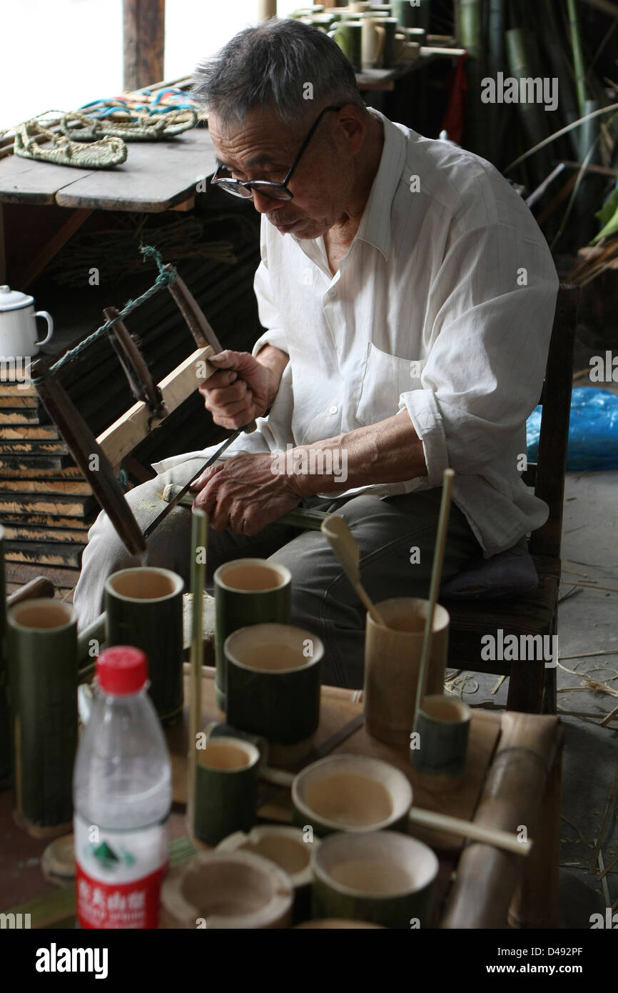 Un anziano uomo cinese utilizza i tradizionali strumenti e metodi per la costruzione di souvenir turistici Il nostro di bambù. Foto Stock