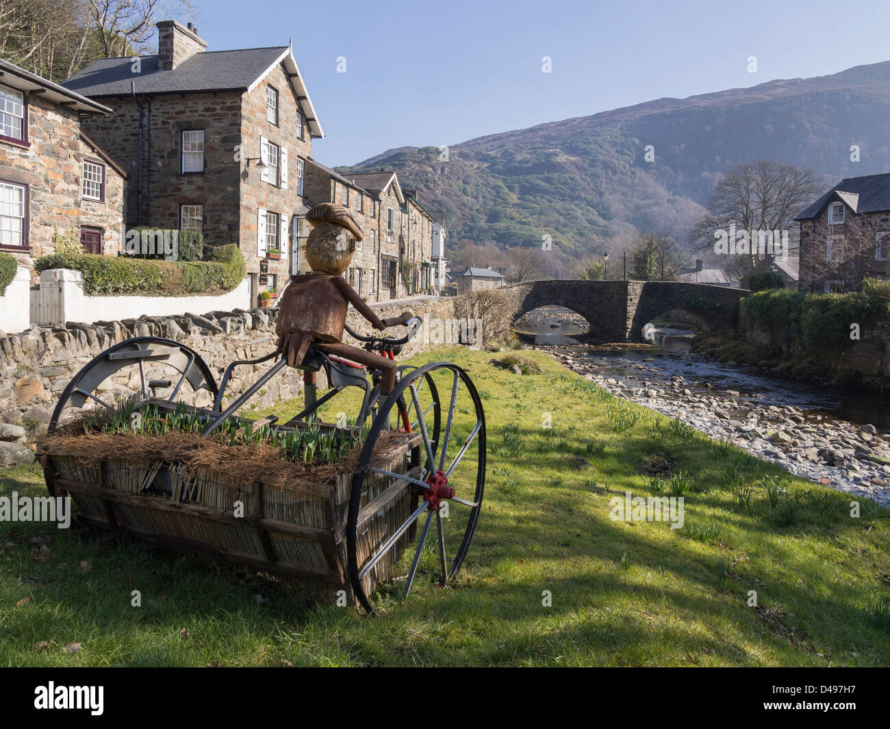 Vista lungo Afon Colwyn fiume al ponte vecchio con inusuale triciclo piantatrice di fiori su riverside in Beddgelert, Snowdonia, Wales, Regno Unito Foto Stock
