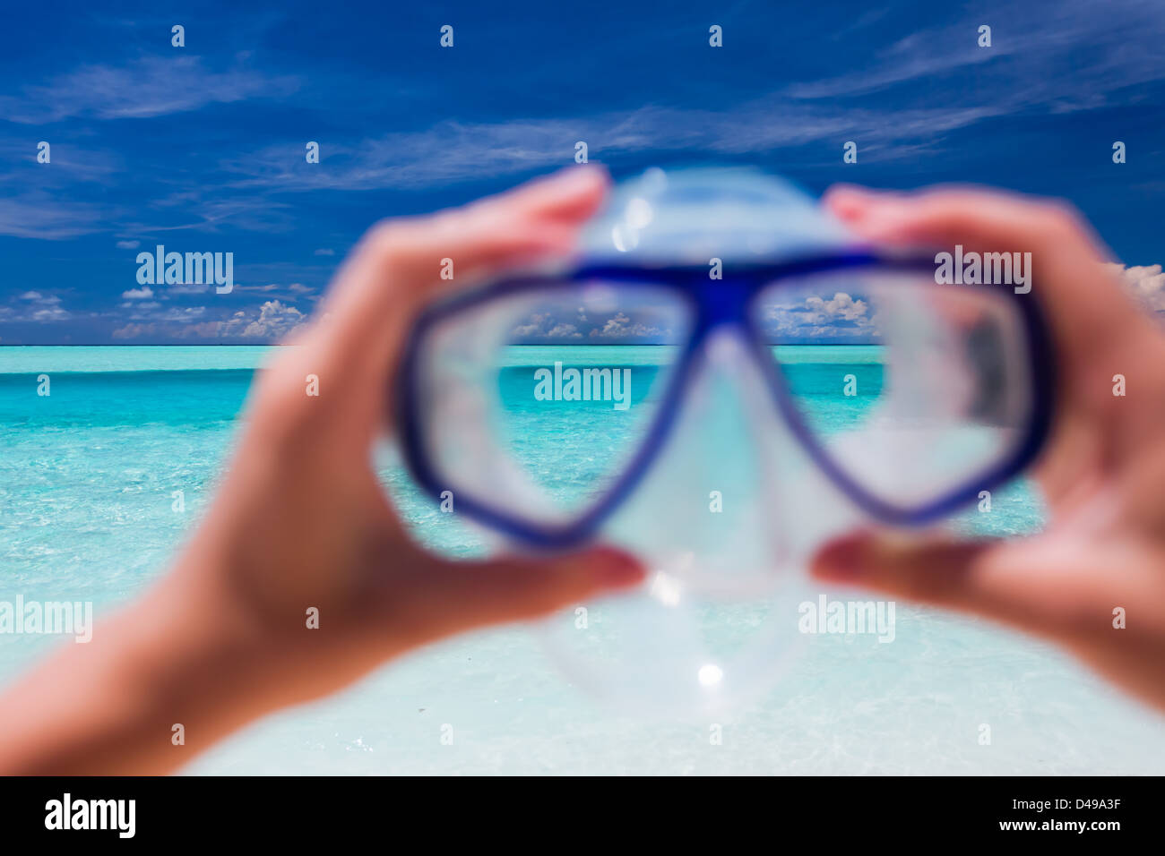 Mano che tiene lo snorkel occhiali protettivi contro la spiaggia tropicale e cielo Foto Stock