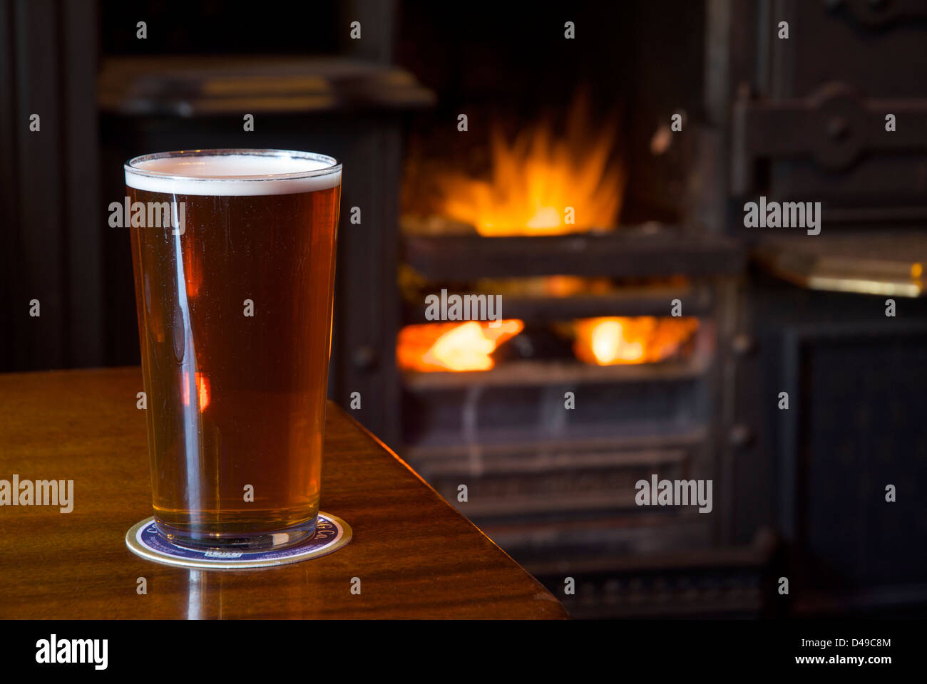 Una pinta di bitter su una tabella pub, con un fuoco aperto in background Foto Stock