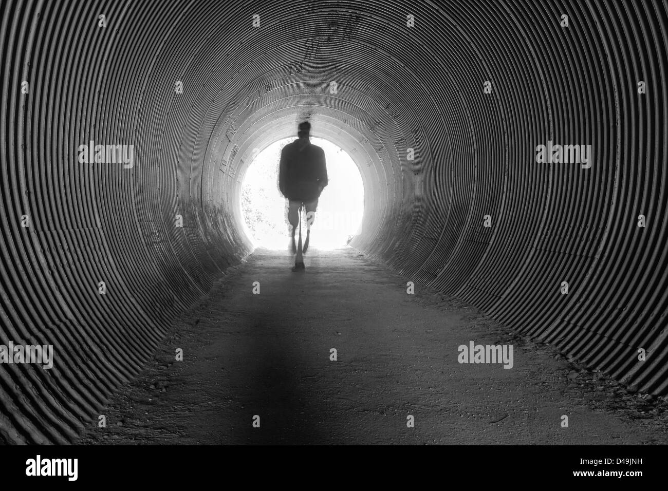 Un singolo uomo cammina attraverso un lungo tunnel nella luce dell'ignoto. Foto Stock