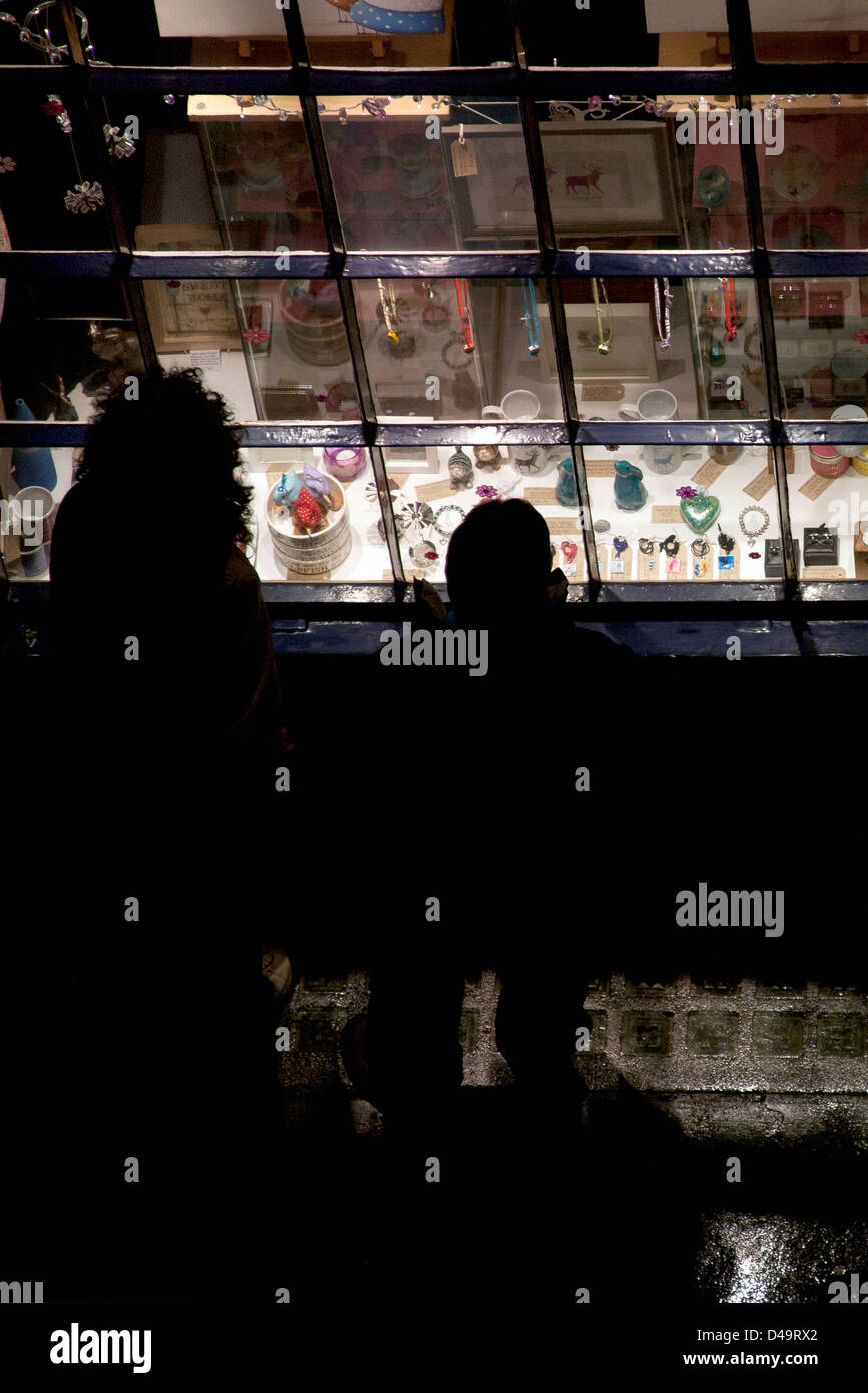 Due persone in cerca di un luminoso negozio finestra a notte alta Petergate, York, Yorkshire England Regno Unito Foto Stock