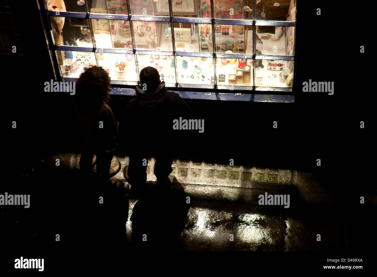 Due persone in cerca di un luminoso negozio finestra a notte alta Petergate, York, Yorkshire England Regno Unito Foto Stock