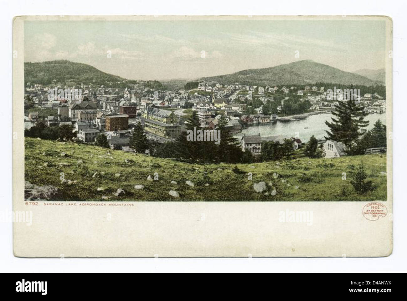 Questa cartolina, risalente al 1902, mostra una vista panoramica del lago Saranac a New York. L'immagine mette in risalto la bellezza naturale della città e il suo sviluppo come popolare destinazione turistica nelle Adirondacks durante l'inizio del XX secolo. Foto Stock