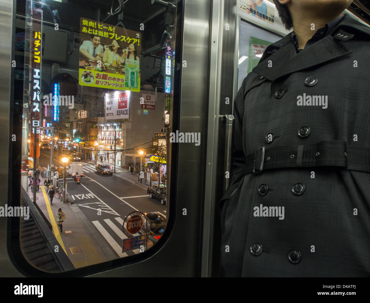 Uomo in un trench coat, un passeggero su una linea Yamanote treno dei pendolari elevati al di sopra di un affollato notte tempo street, stazione Shin-Okubo, Tokyo, Giappone. Foto Stock