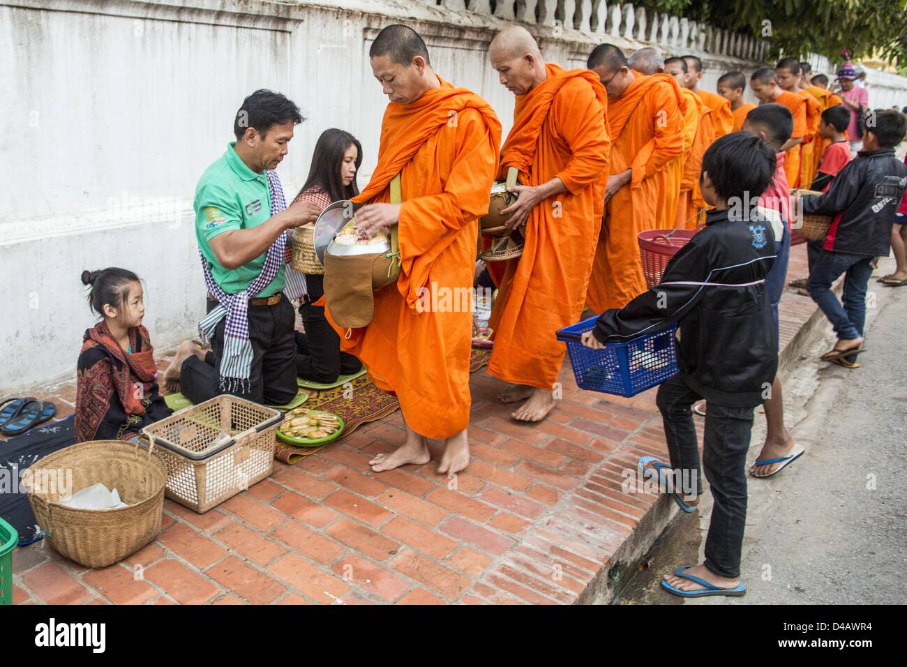 Luang Prabang, Laos. Undicesimo Marzo 2013. I monaci buddisti raccogliere elemosine durante il tak bat in Luang Prabang. ''Tak Bat'' è un rito quotidiano nella maggior parte del Laos (e altri buddista Theravada paesi come la Thailandia e Cambogia). I monaci di lasciare i loro templi all'alba e cammina silenziosamente attraverso le strade e le persone di mettere il riso e altri prodotti alimentari nella loro alms a bocce. Luang Prabang, nel nord del Laos, è particolarmente conosciuto per la mattina ''tak bat'' a causa del grande numero dei templi e dei monaci in città. lms da persone Credito: ZUMA Press, Inc. / Alamy Live News Foto Stock