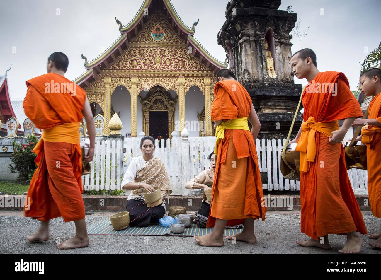 Luang Prabang, Laos. Undicesimo Marzo 2013. I monaci buddisti a piedi passato Wat Nong Sikhounmuang e raccogliere elemosine durante il tak bat in Luang Prabang. ''Tak Bat'' è un rito quotidiano nella maggior parte del Laos (e altri buddista Theravada paesi come la Thailandia e Cambogia). I monaci di lasciare i loro templi all'alba e cammina silenziosamente attraverso le strade e le persone di mettere il riso e altri prodotti alimentari nella loro alms a bocce. Luang Prabang, nel nord del Laos, è particolarmente conosciuto per la mattina ''tak bat'' a causa del grande numero dei templi e dei monaci nella città Credito: ZUMA Press, Inc. / Alamy Live News Foto Stock