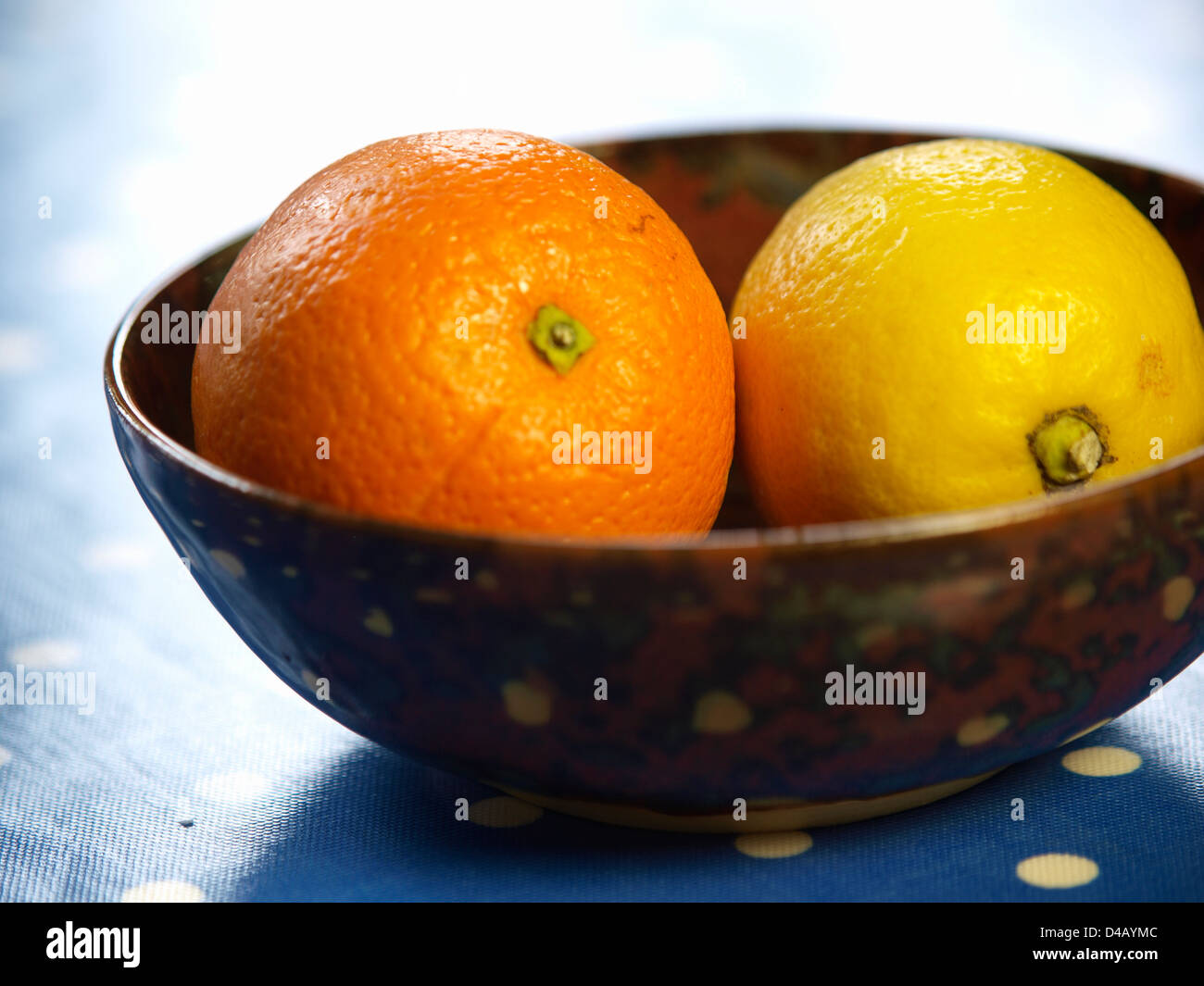 Un'arancia e di limone in una ciotola su una tabella con macchiato il panno della tabella Foto Stock