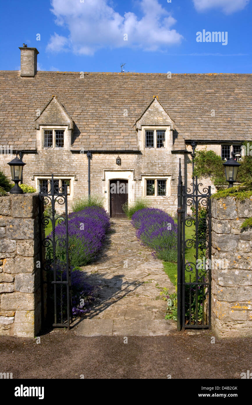 Un open garden gate e lavanda percorso alberato che conduce a un idilliaco Cotswold cottage in pietra, Gloucestershire, England, Regno Unito Foto Stock