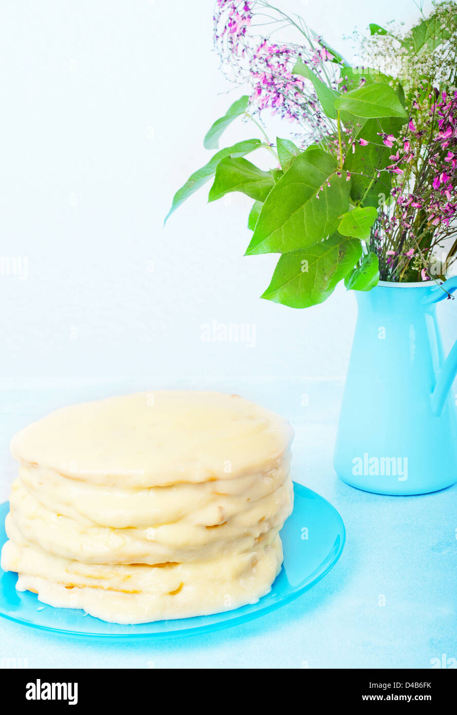 Lo strato di fatti in casa la torta su un piatto di colore blu, sfondo blu vaso con un mazzo di fiori Foto Stock