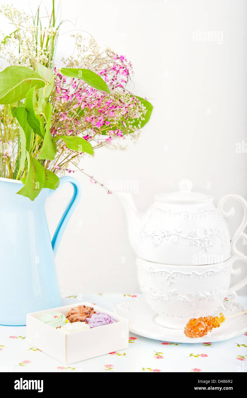 Tazza bianca e teiera, quattro caramelle colorate, zucchero e stick fiori in una brocca blu Foto Stock