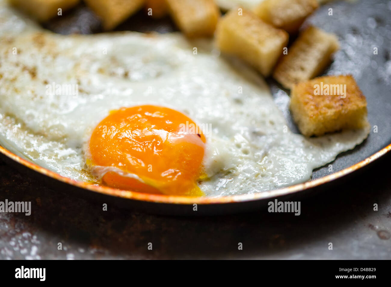 Padella piena di le uova strapazzate da due uova con piccoli pezzi di pane tostato. Si erge su grunge sfondo di metallo. Foto Stock