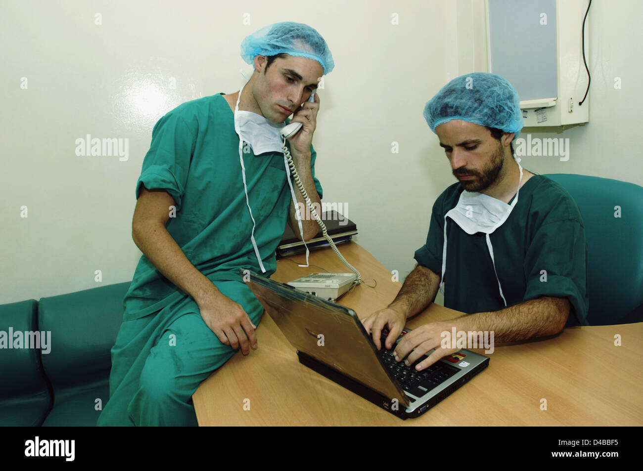 Due chirurgo discutere dettagli paziente per telefono e aggiornare i dettagli sul computer portatile Foto Stock