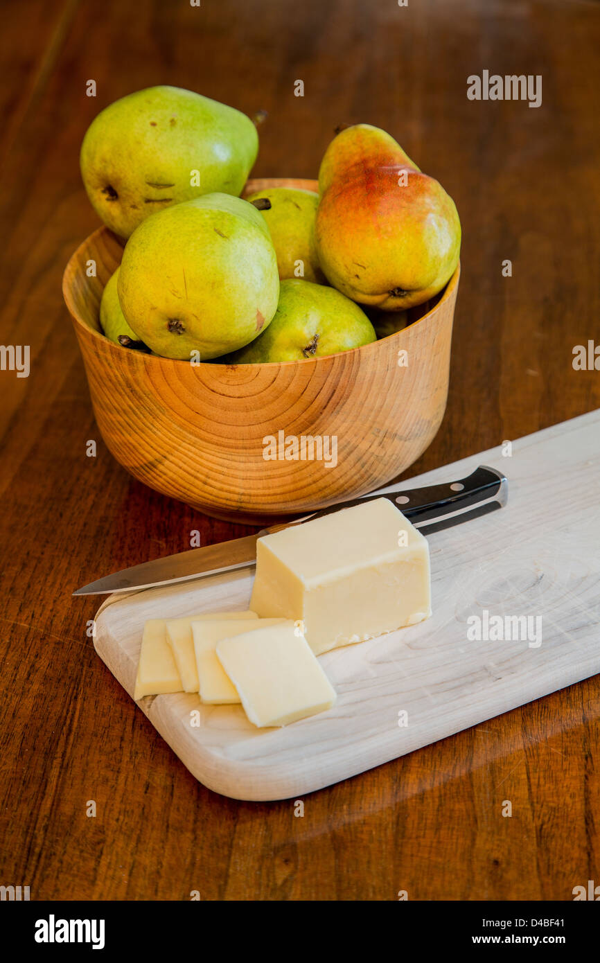 Una ciotola di fresco Bartlett pere su una tavola di legno con formaggio a fette e un coltello seghettato su un legno tagliere Foto Stock