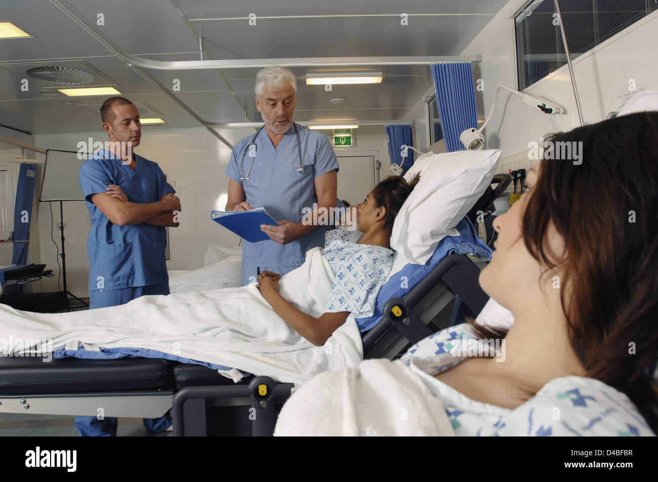 I medici sono il controllo della salute del paziente come shes che stabilisce nel letto di ospedale Foto Stock