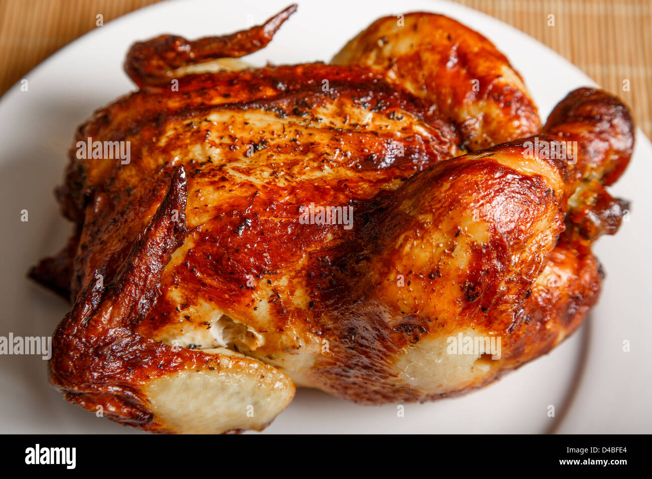 Un intero pollo arrosto su una piastra bianca e bambù placemat Foto Stock