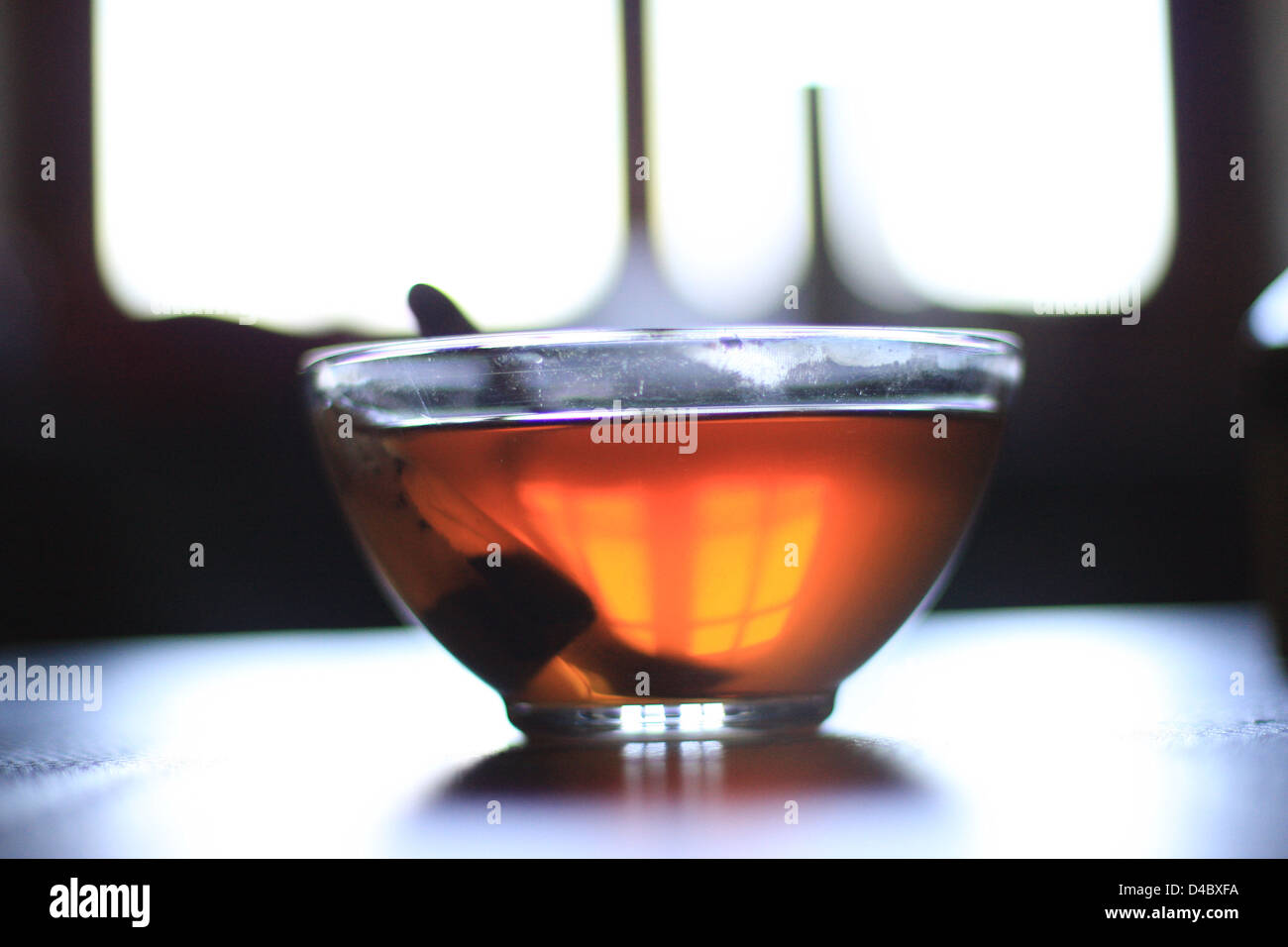 Una tazza di tè si siede su una tabella che riflette la luce e trasformare la finestra dietro di essa Foto Stock