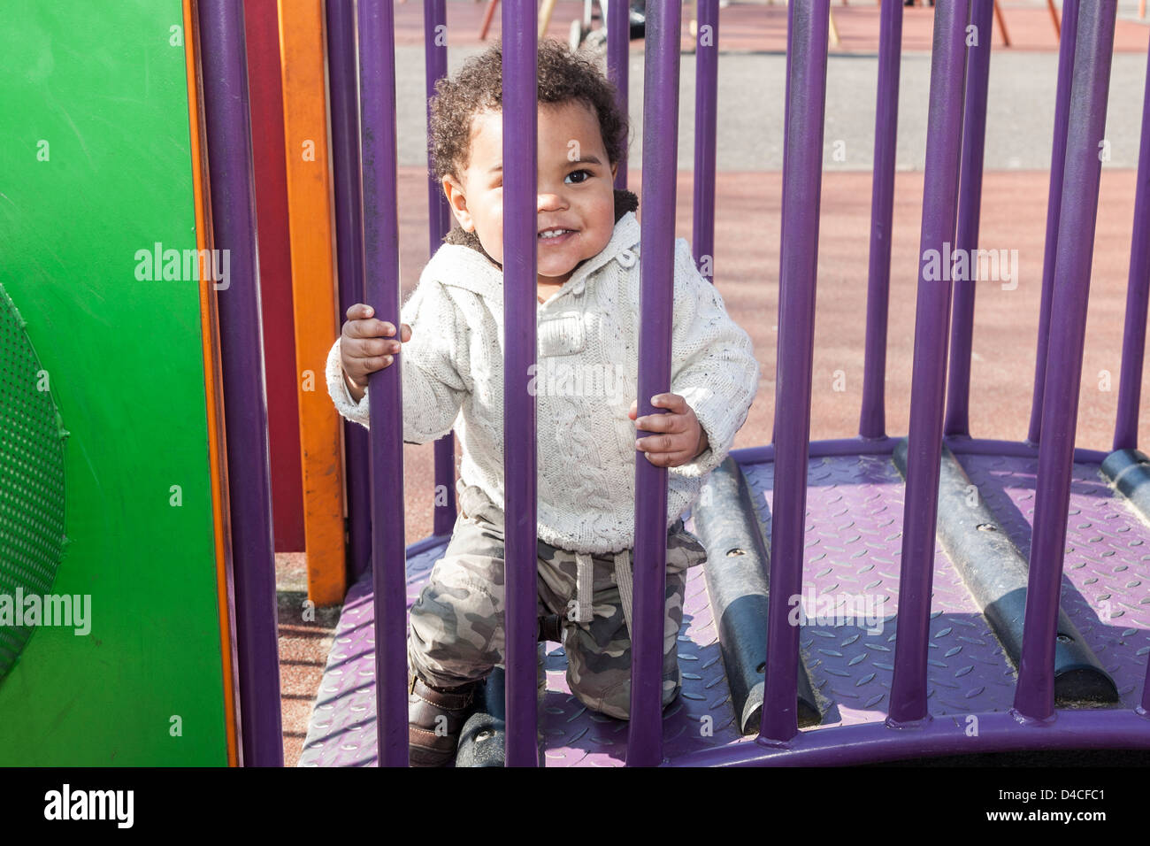 Razza mista toddler boy visto attraverso viola le ringhiere del telaio di arrampicata di ridere Foto Stock