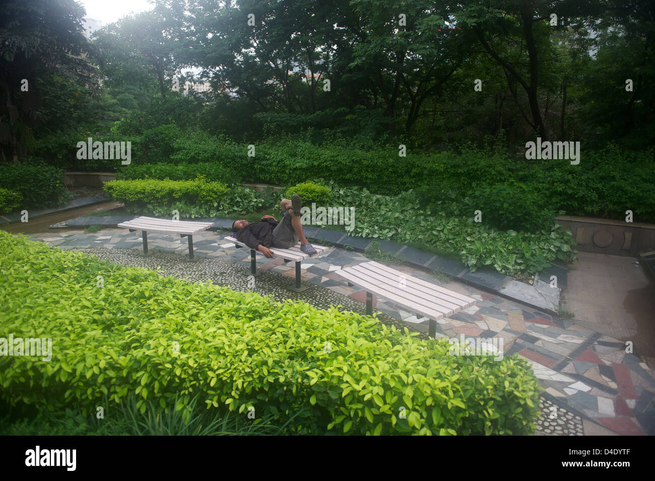 Nanning pomeriggio,un mendicante senzatetto approfittando del pranzo sun relax su una panchina in un parco nel centro della città Foto Stock