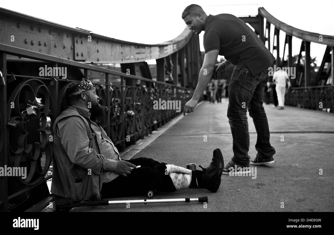 Giovane uomo dando cambiare per un vecchio senzatetto uomo seduto sul pavimento sul ponte di amore a Francoforte in Germania. Foto Stock