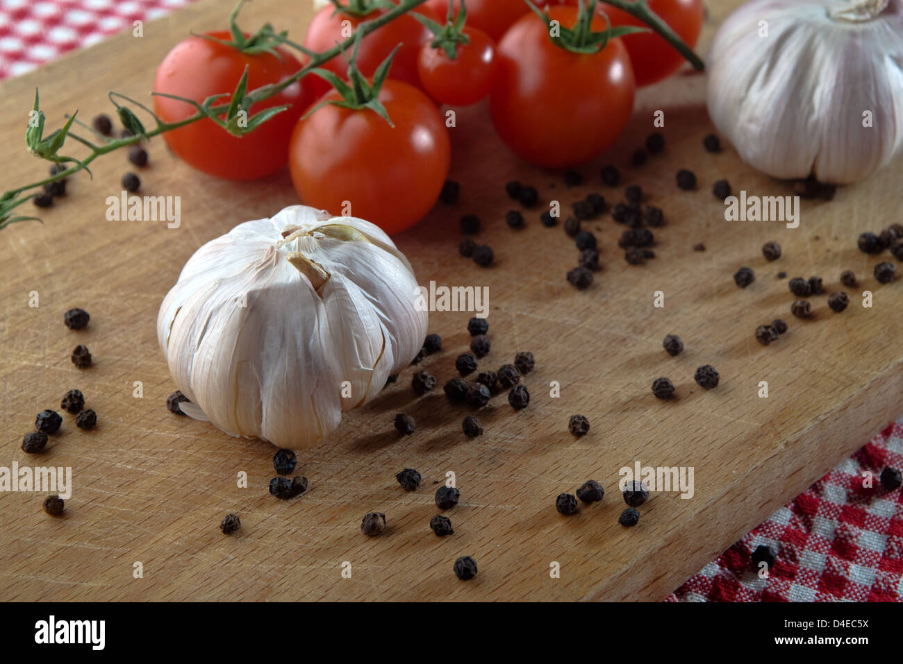 L'aglio, il pomodoro ciliegino e pepe sementi sul piatto di legno sul tavolo da cucina. cibo sano sfondo. Foto Stock