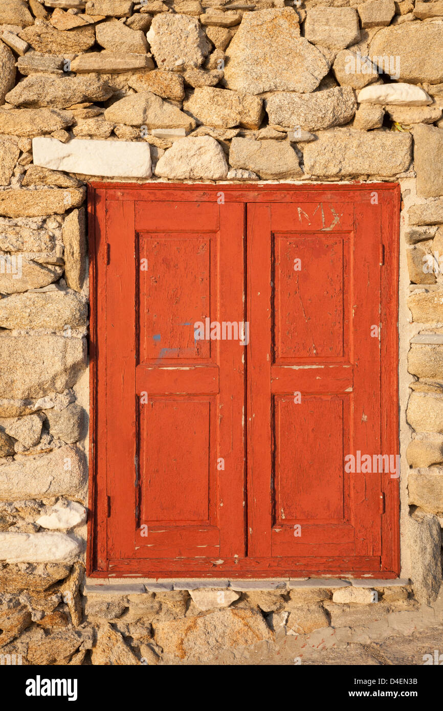 Persiane di legno rosso intemperie in un edificio in pietra sull'isola greca di Mykonos Foto Stock